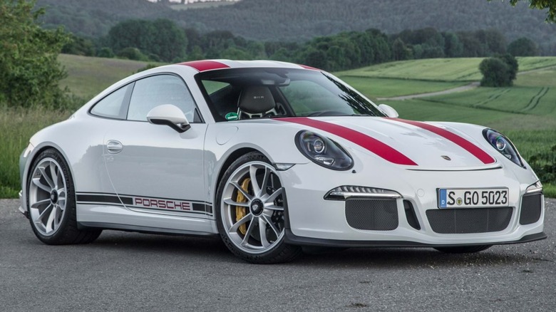 A white Porsche 911R with red stripes with fields and trees in the background