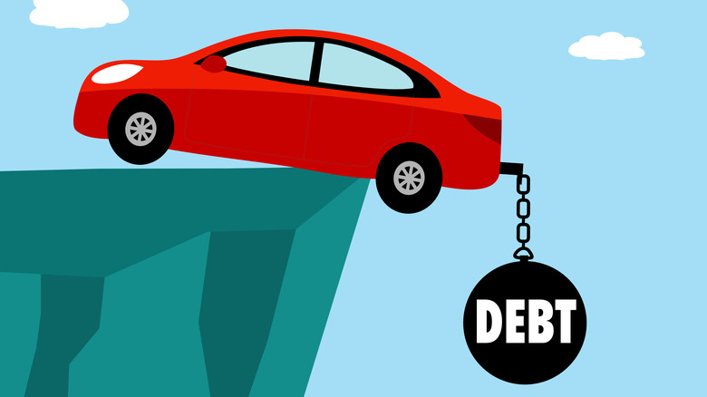 A cartoonish red car precarious balances on the edge of a cliff with a large ball reading "debt" and chain attached to its trailer hitch.