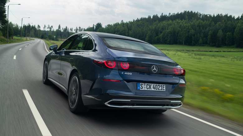 A dark blue electric Mercedes-Benz C-Class speeding down a forest road