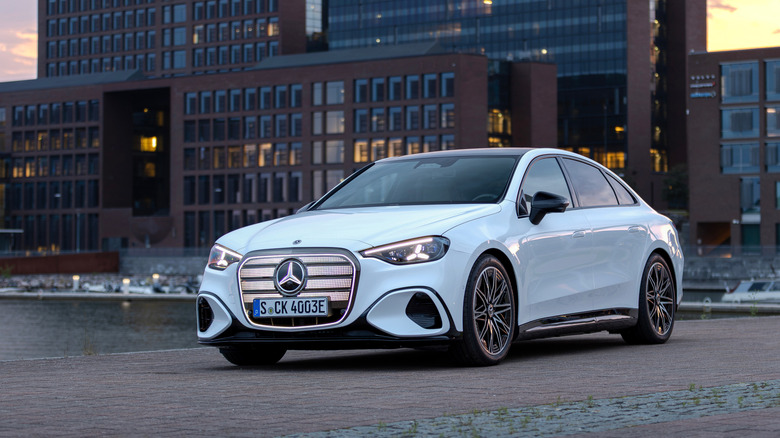 A white electric Mercedes-Benz C-Class parked in front of a cityscape at sunset