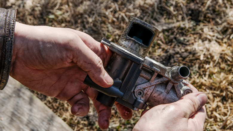 A close-up of a person's hands holding an EGR valve.