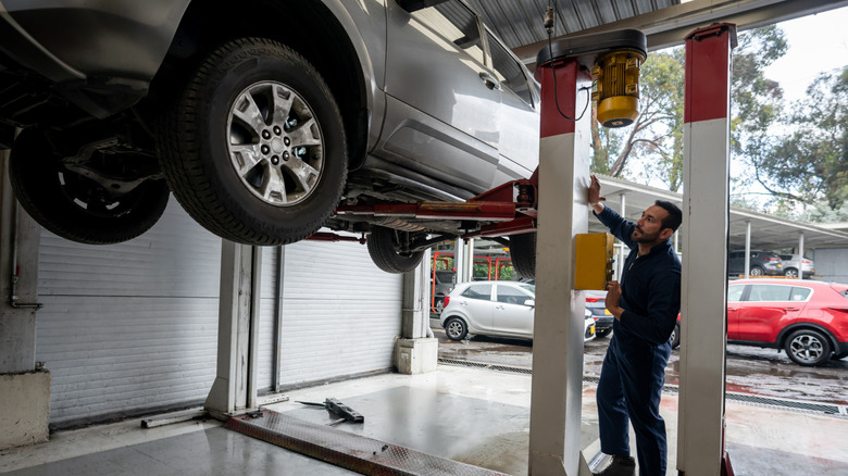 Latin American mechanic lifting a car on a lift at an auto repair shop to fix it - vehicle breakdown concepts