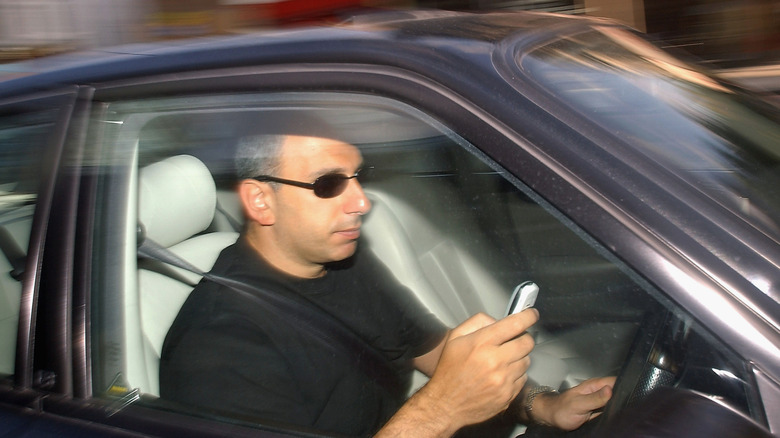a man writes a text message on his mobile phone whilst driving in London