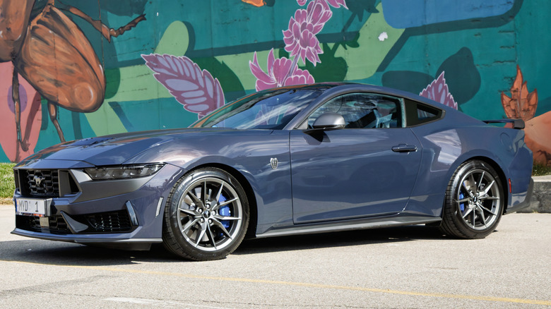 A dark gray S650 generation Ford Mustang Dark Horse parked in front of a graffiti wall.