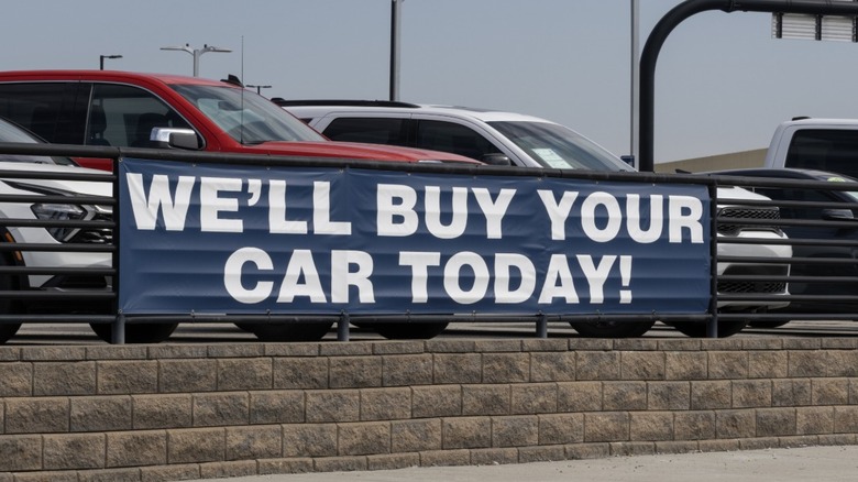 A sign at a car dealership that says, "We'll buy your car today!"